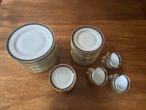 A neatly arranged set of white and blue bordered china dishes, including stacks of plates, bowls, and several teacups with saucers, on a wooden table.