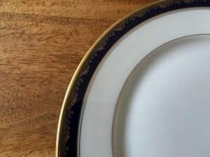 Close-up of a decorative china plate with a gold and black patterned rim on a wooden surface.