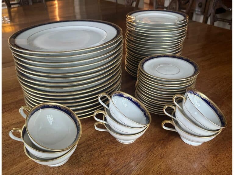 A collection of stacked white porcelain plates and cups with gold and blue trim on a wooden table.