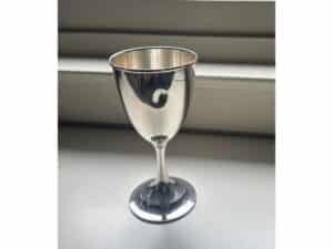 A shiny silver chalice with a decorative swirl on its bowl rests on a white surface.