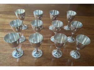 Twelve silver goblets arranged on a wooden surface.