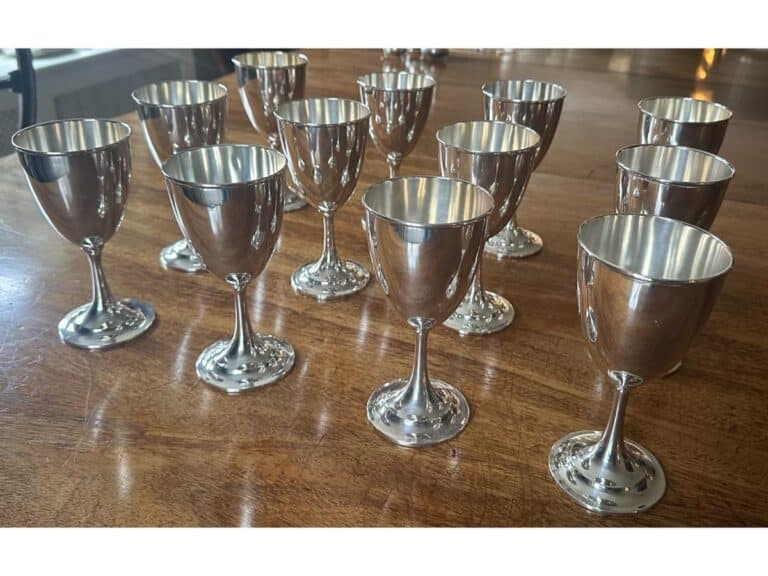 A set of twelve shiny silver goblets are neatly arranged on a wooden table.