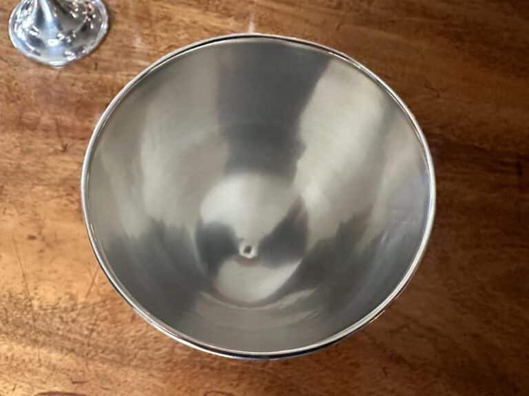 A shiny, empty metal mixing bowl on a wooden surface, viewed from above.