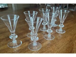 Seven clear glass goblets with decorative stems are arranged on a wooden table.