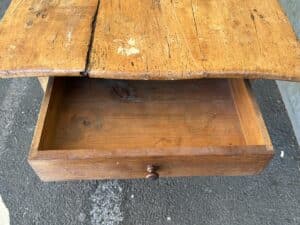 Open wooden drawer beneath a rustic wooden tabletop on a textured surface.