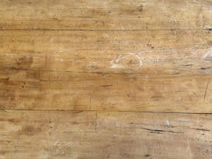 Close-up of a scratched and stained wooden surface with visible grain and circular marks.