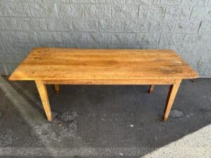 A wooden table with four legs stands on a concrete surface against a brick wall.