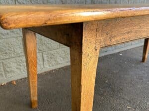 Close-up of a wooden table with a textured surface, positioned on a concrete floor against a green brick wall.