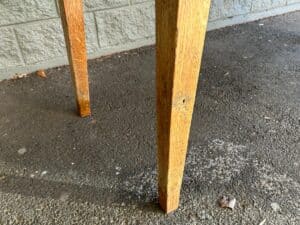 Close-up of wooden table legs on a textured concrete surface, with a brick wall in the background.