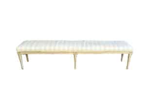 An Antique Upholstered Swedish Style Bench featuring light striped fabric and wooden legs.