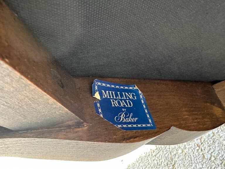 A wooden furniture piece with a partially torn blue label reading "Milling Road by Baker.