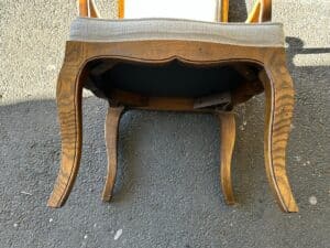 An upside-down wooden chair with a light-colored cushioned seat on a textured asphalt surface.