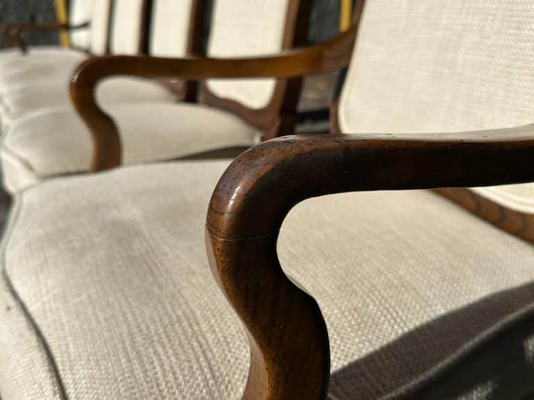 A row of chairs with light fabric seats and wooden armrests in sunlight.