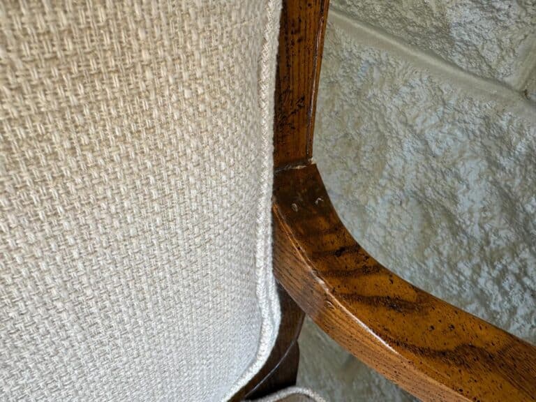 Close-up of a wooden chair frame with beige textured upholstery against a stone wall.