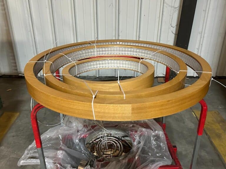 Wooden spiral structure resting on a red cart in front of a corrugated metal wall.