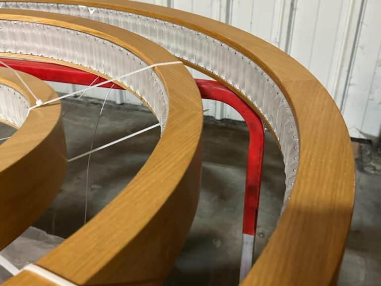 Close-up of circular wooden structures with red supports and white cords, set against a gray industrial background.