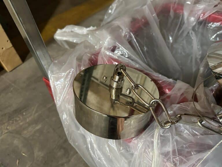 Close-up of a metal weight with a chain attached, placed on a surface covered with transparent plastic.