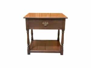 The English Traditions Bedside Table is a wooden side table with one drawer, an ornate handle, and a lower shelf supported by four turned legs.