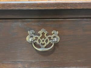 Ornate brass drawer pull on a dark wooden surface.