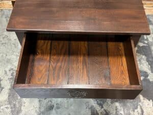 Open wooden drawer with a decorative metal handle on a worn floor.