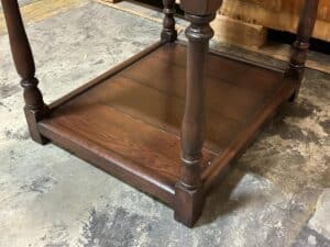 Wooden table with ornate legs and a lower shelf, viewed from a low angle on a concrete floor.