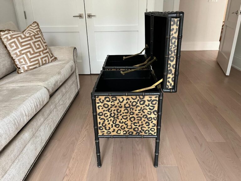 A leopard print storage bench with open compartments stands on a wooden floor next to a beige sofa with patterned cushions.