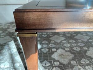 Close-up of a wooden table corner with a brass accent on the leg, set against a patterned carpet.