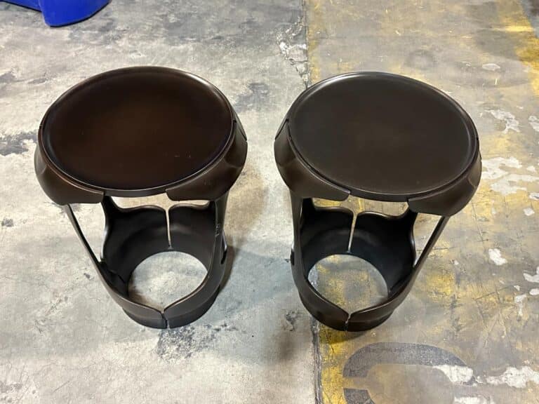 Two black cylindrical stools with open sides and circular tops on a concrete floor.