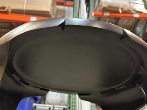 Close-up view of a black circular object with visible jagged edges, set in a warehouse environment with shelves and boxes in the background.