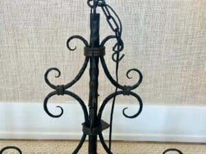 Close-up of a black wrought iron chandelier with scrollwork design against a beige textured background.