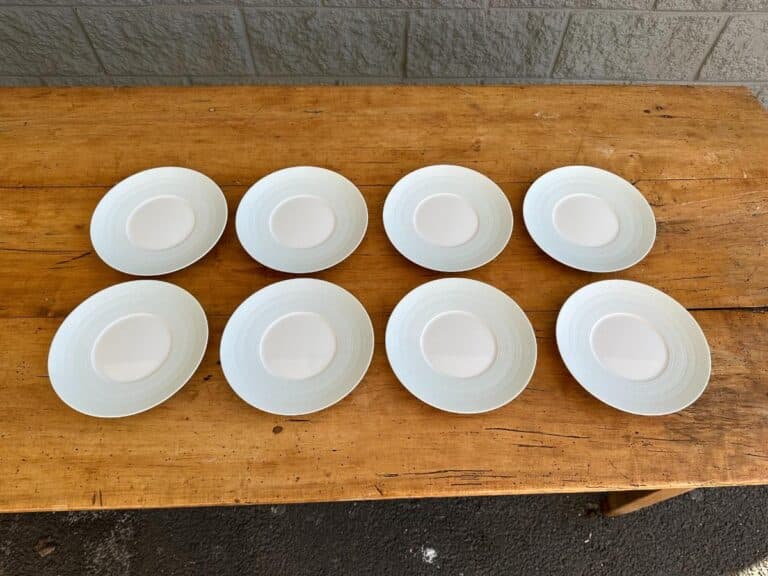 Eight white saucers arranged in two rows on a wooden table.