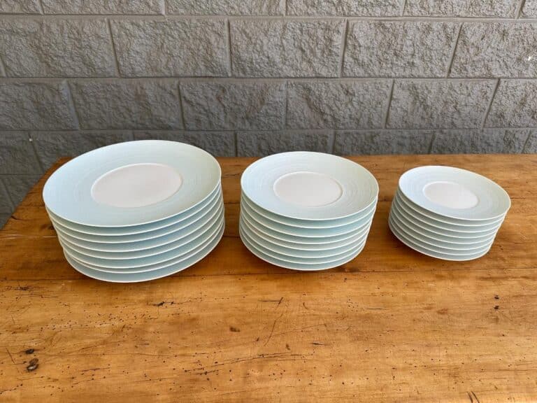 Three stacks of white plates on a wooden table, arranged from largest to smallest. Background features a gray brick wall.