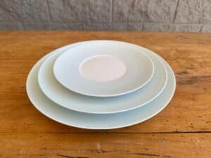 Three light blue ceramic plates of varying sizes stacked on a wooden surface.