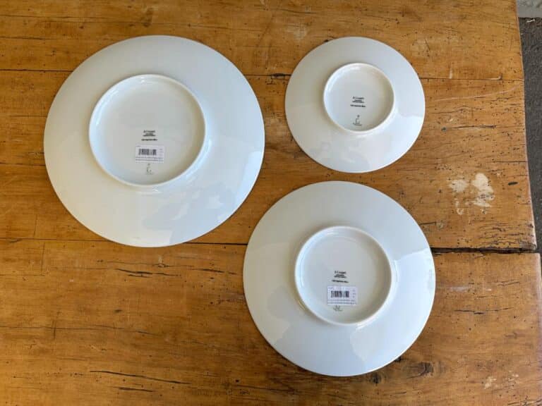 Three white plates of varying sizes are displayed upside down on a wooden surface, each with a barcode sticker.