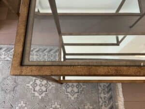 Close-up of a glass-top table with a metallic frame, placed on a patterned rug.