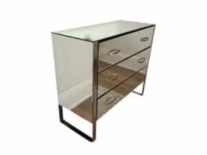 The Modern Mirrored Dresser, featuring three drawers with metal handles, stands elegantly on a wooden floor.