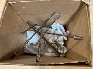 A cardboard box containing disassembled metal rods and fixtures with a white cloth inside.