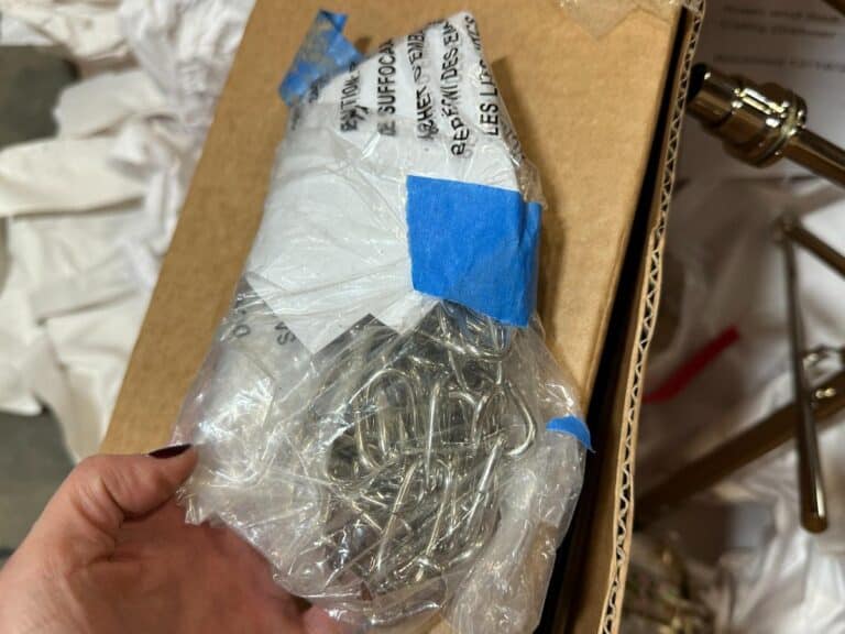 A hand holding a clear plastic bag containing metal hooks, placed on a cardboard box.