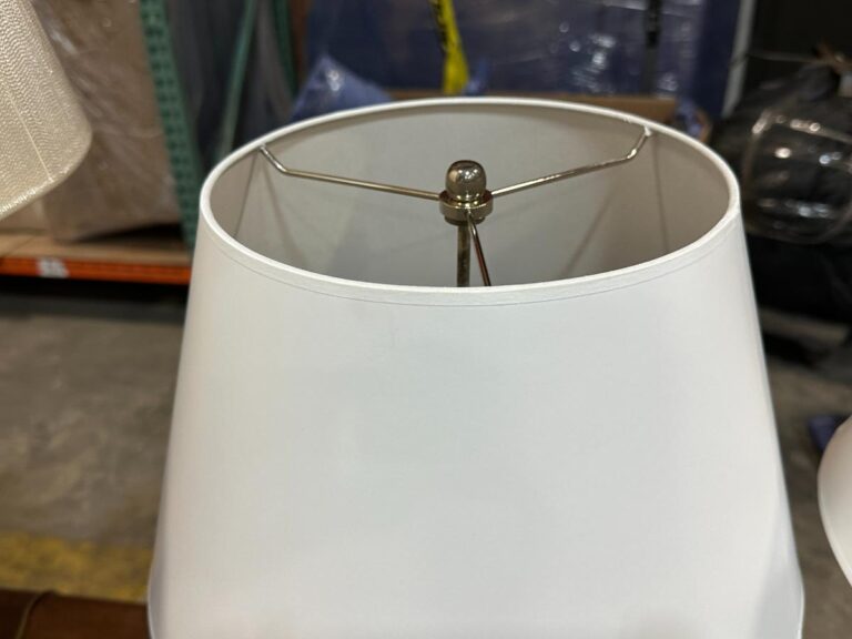 Close-up of a white lamp shade with a metal spider fitter, situated in a warehouse setting.