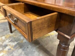 A wooden table with an open drawer displaying brass handles, standing on a stone floor.