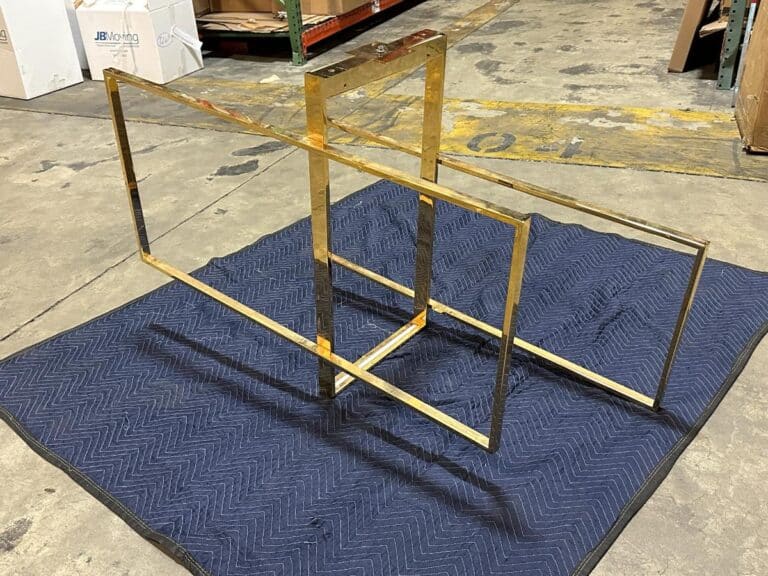 A geometric metal frame sculpture sits on a quilted blue mat in a warehouse environment.