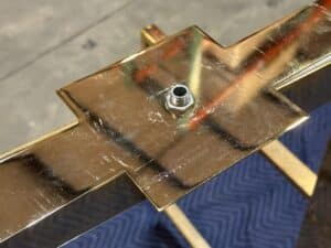 A close-up of a metallic, golden structure with a hexagonal bolt inserted in the center, on a patterned dark blue surface.