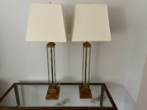 Two identical table lamps with square beige shades sit on a glass-top table against a white wall.