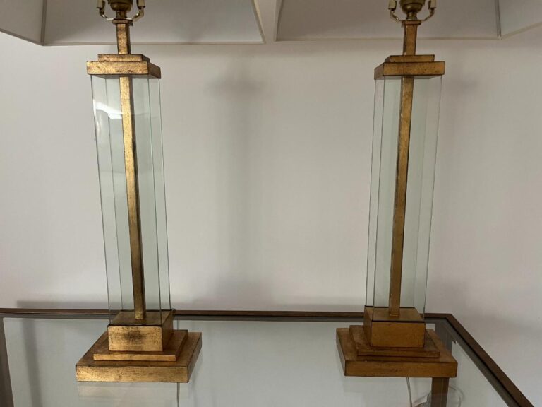 Two tall rectangular lamps with clear glass frames and gold accents sit on a glass table.