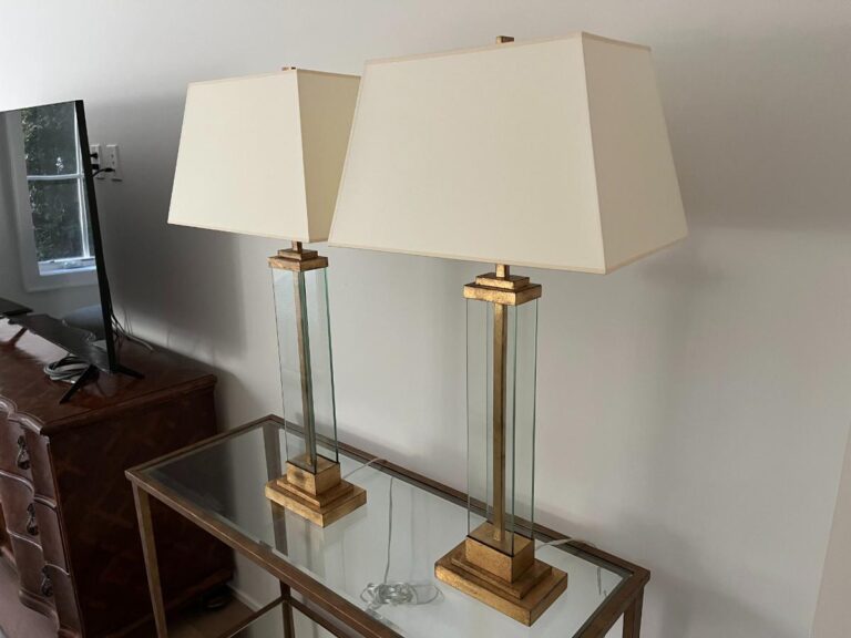 Two elegant table lamps with square beige shades on a glass-top side table, next to a TV.