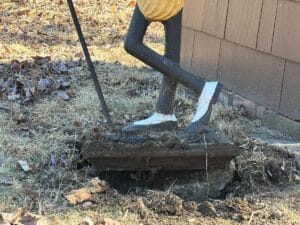 The legs of the Cast Iron "Life Size" Mr. Peanut Statue, clad in shoes, dig into the ground with brown house siding in the background.