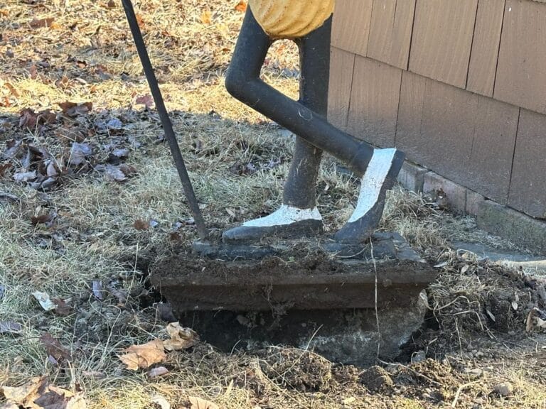 The legs of the Cast Iron "Life Size" Mr. Peanut Statue, clad in shoes, dig into the ground with brown house siding in the background.
