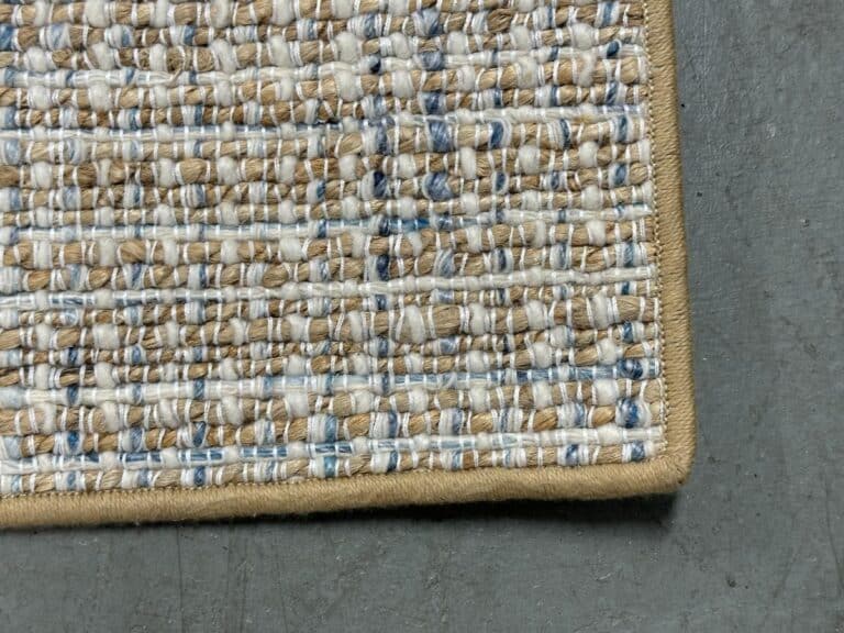 Close-up of the corner of an 8 x 9 Tan, Light Blue & White Area Rug on a gray concrete floor.