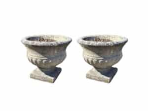 A pair of stone garden urns planters with ornate designs are set side by side on a white background.