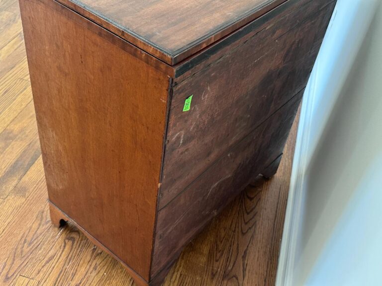 Bachelor's Chest of Drawers, adorned with a small green price tag, set against a white wall on a hardwood floor.